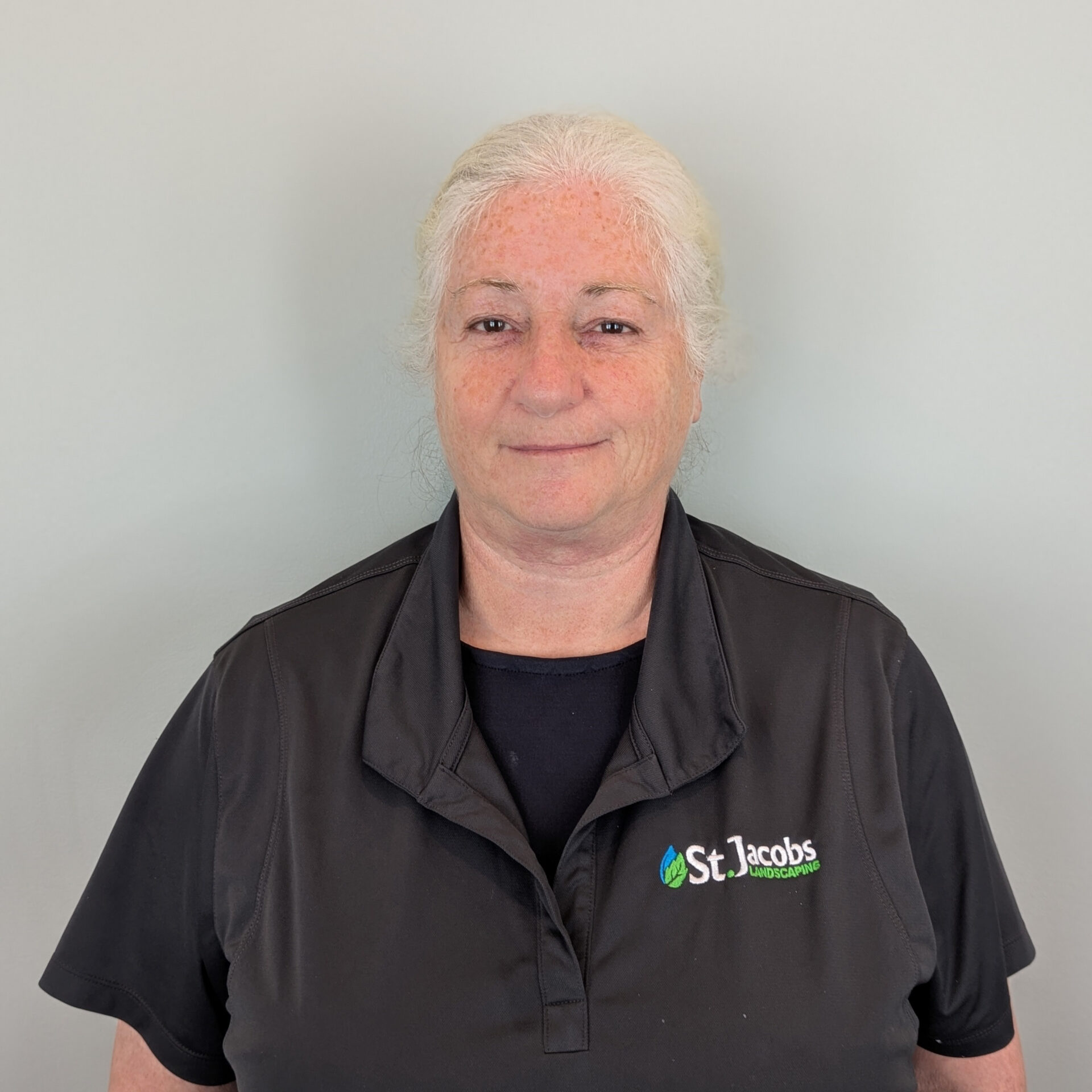 A person with gray hair stands against a neutral background, wearing a black shirt with the logo "St. Jacobs Landscaping".