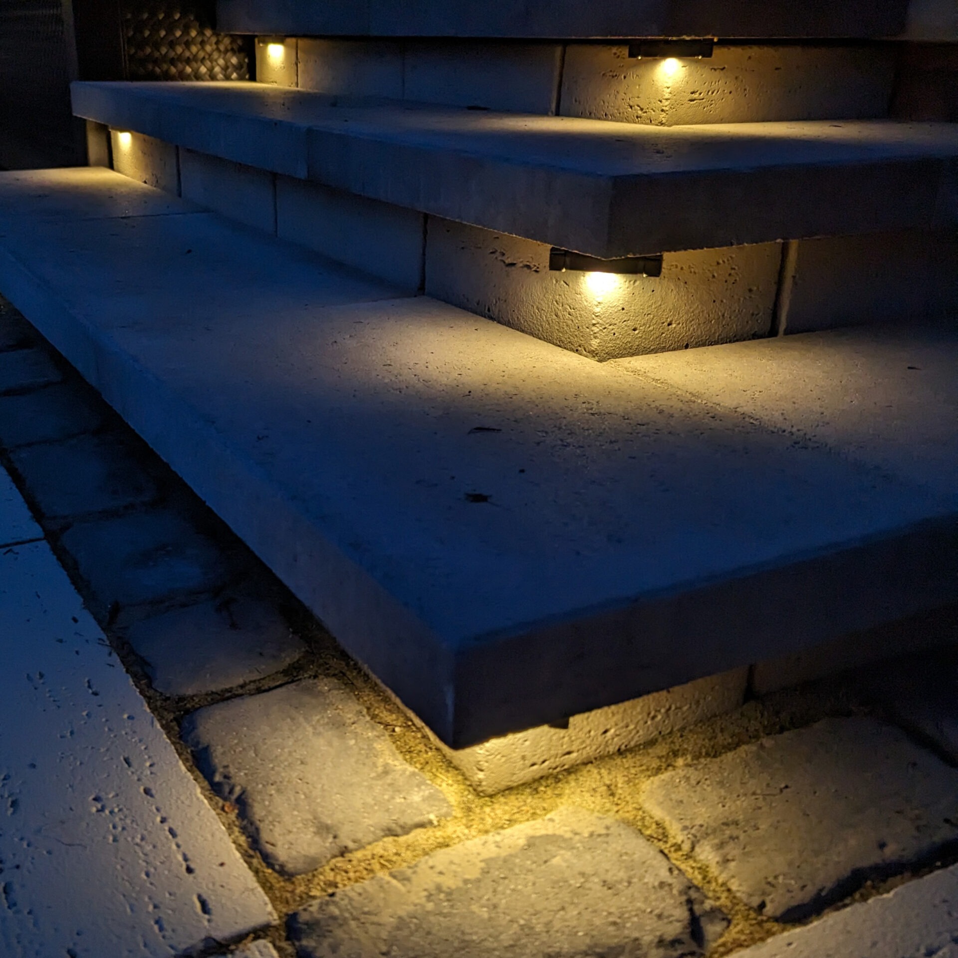 Stone steps illuminated by small recessed lights at night, casting a warm glow on the ground and creating a serene atmosphere.