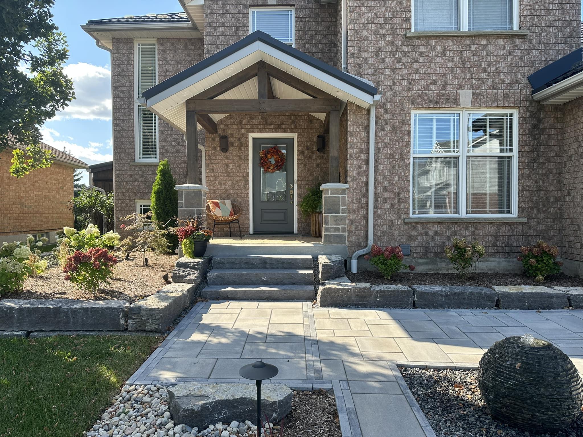 Front entry of a brick home with timber‑post porch, stone steps, paver walkway, and round water feature.