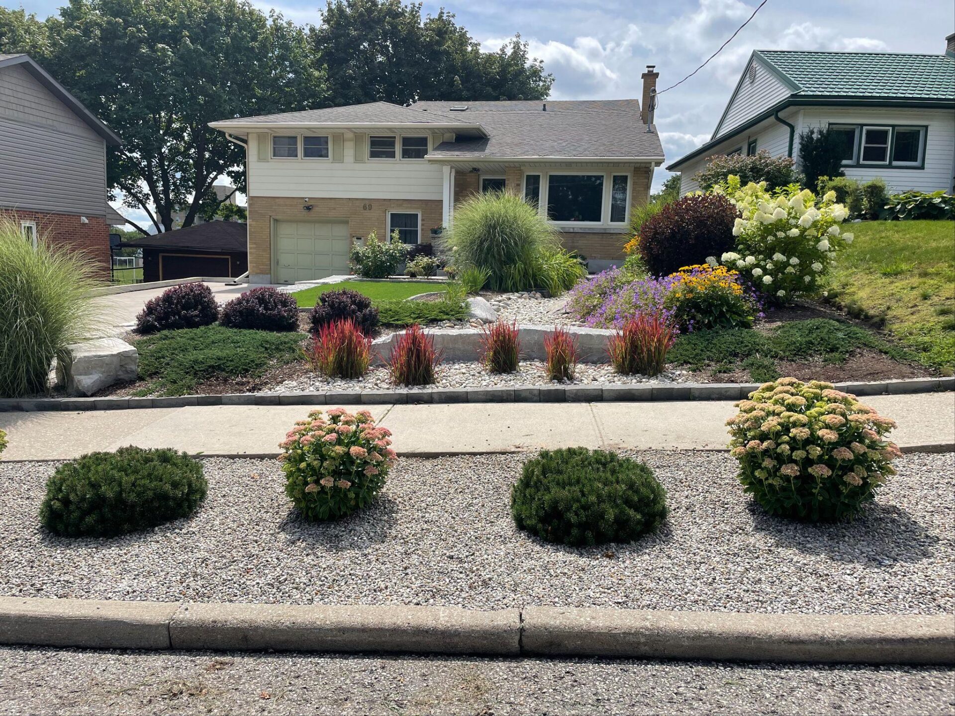 Sloped front yard with colorful shrubs and grasses around a dry creek bed at a split‑level home.